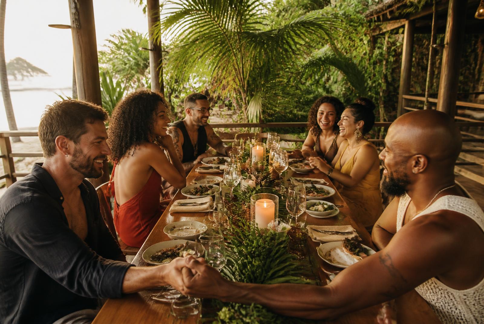 A group of LGBTQ+ friends sharing a long candlelit dinner on an open-air jungle terrace